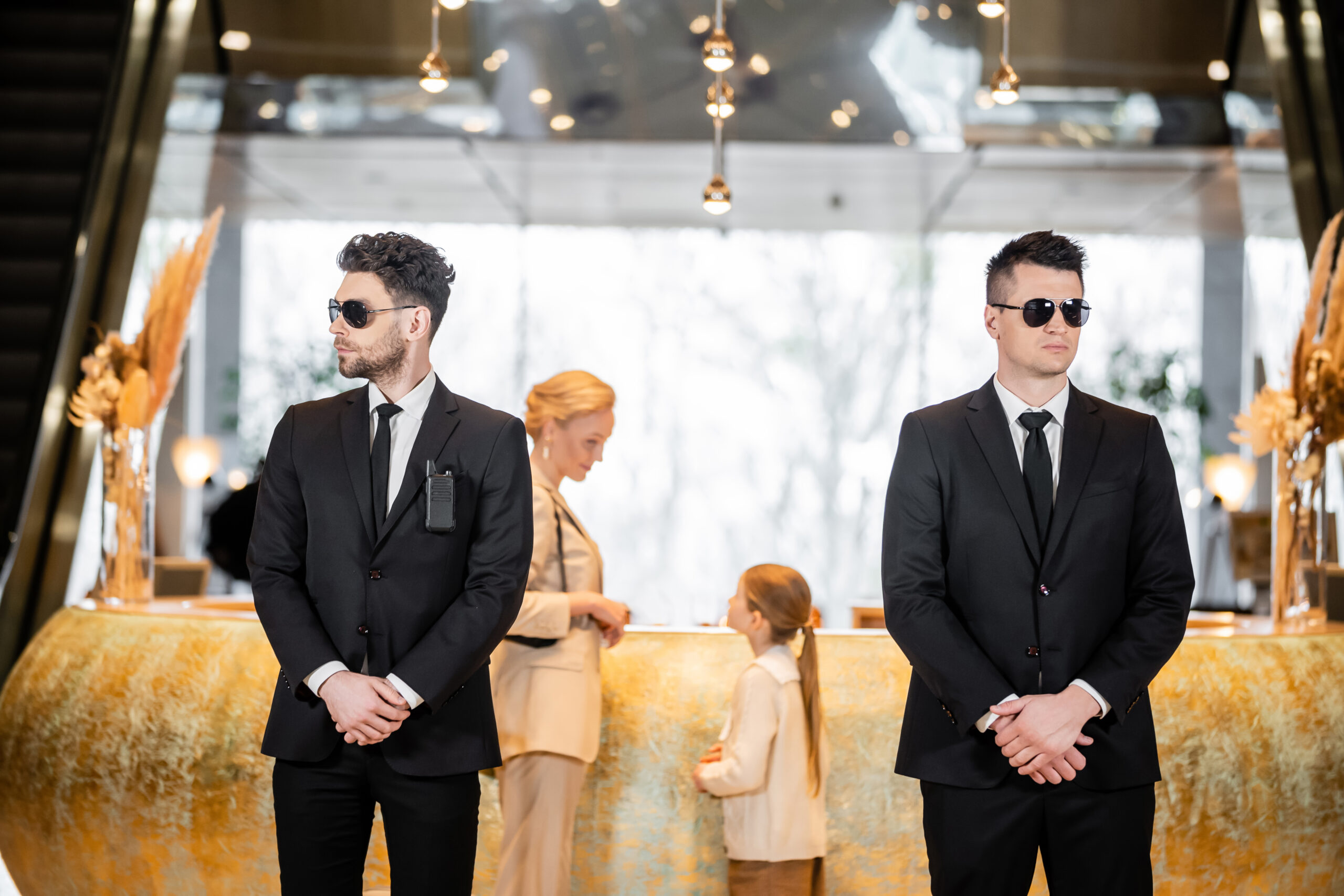 personal security, handsome bodyguards in suits and sunglasses protecting mother and child in hotel lobby, luxury lifestyle, woman and girl standing at reception desk